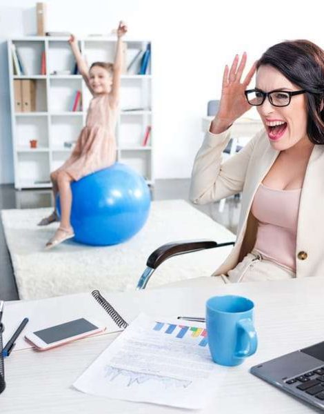 stressed businesswoman yelling in office daughter sitting on fitness ball behind