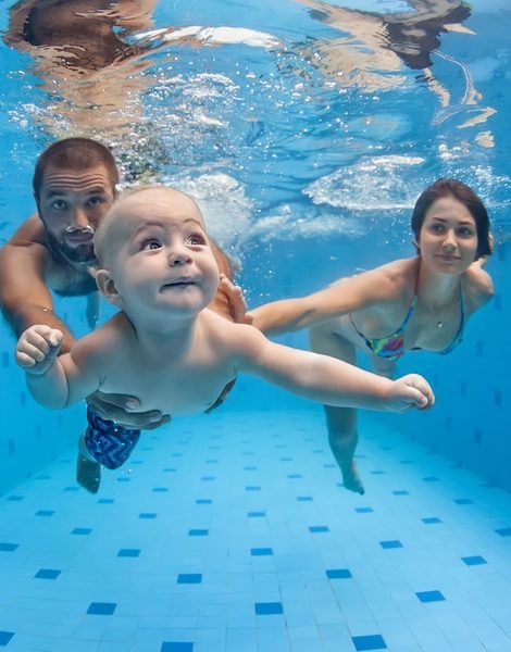 Happy full family - mother father baby son learn to swim dive underwater with fun in pool to keep fit. Healthy lifestyle active parent people water sport activity swimming lesson. Focus on child