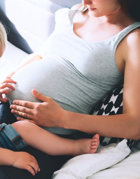Pregnant mother and son are talking and spending time together in bed at home. Little child boy looking at her mother pregnant tummy. Pregnancy family parenthood preparation and expectation concepts.