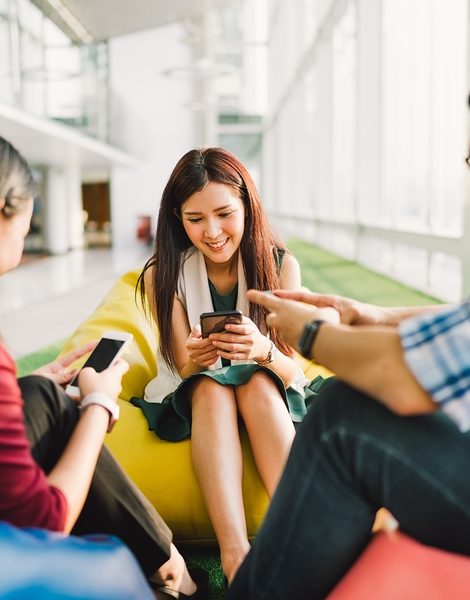 Three Asian college students or coworkers using smartphones together. Fun modern lifestyle social network or communication technology gadget concept focus on middle girl depth of field effect