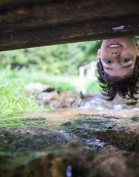 Beautiful fun day for upside down cute little boy on mountain creek in nature