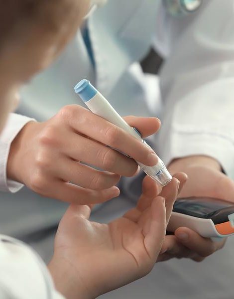 Doctor using lancet pen and digital glucometer to check diabetic boy's blood sugar level, closeup