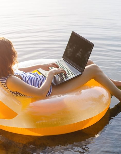 Freelancer works on a laptop sitting in an inflatable ring in the water free space. Business woman working and relaxing on the beach.