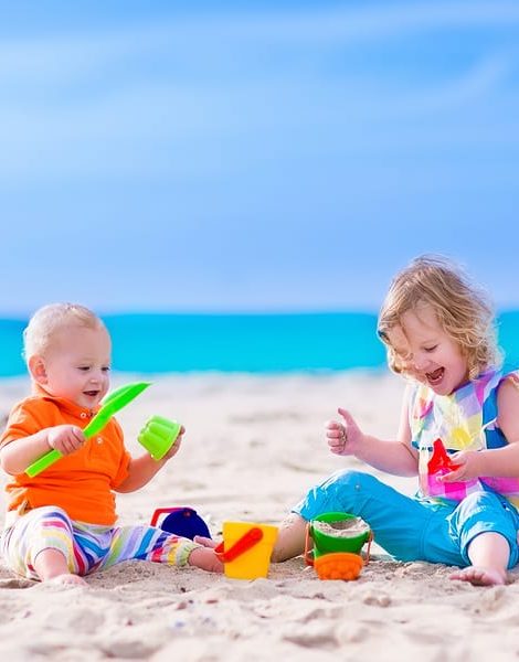 Kids play on a beach. Children building sand castle on tropical island. Summer water fun for family. Boy and girl with toy buckets and spade at the sea shore. Ocean vacation with baby and toddler kid.