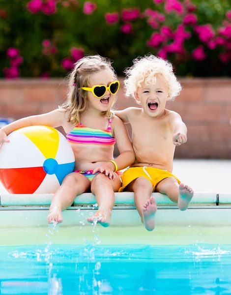 Kids playing at outdoor swimming pool. Little girl and boy play and swim in resort pool on tropical beach island summer family vacation. Swim and eye wear sun protection water toys for children.