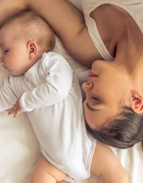 Top view of beautiful young mom and her cute little baby sleeping in bed at home