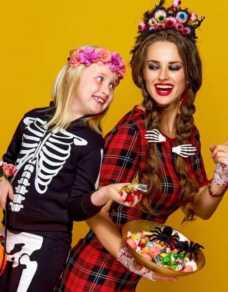 Colorful halloween. smiling modern mother and child in Mexican style halloween costume stealing candies isolated on yellow