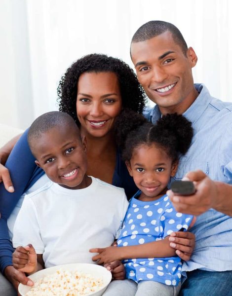 Smiling Afro-american family eating popcorn and watching TV in the living-room