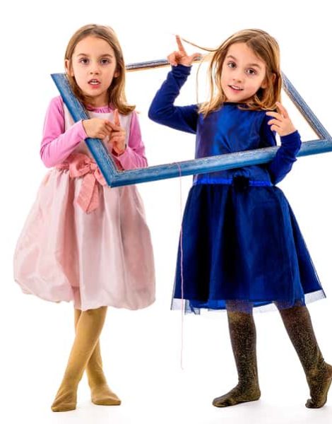 Twin girls are making happy expressions with picture frame. Children posing in studio fooling around making different facial expressions.