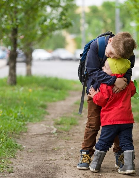 Two little brothers hugging each other when meeting in the park. Cute kid boy meets his little toddler sibling and hugs him. Happy children walking on the road. Lifestyle and family concept
