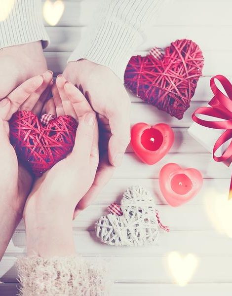 Valentine Gift. Young Couple Hands holding red heart gift over wooden background. St. Valentine's Day, Love concept. Top view, tabletop. Hands in Hands, romance, dating concept