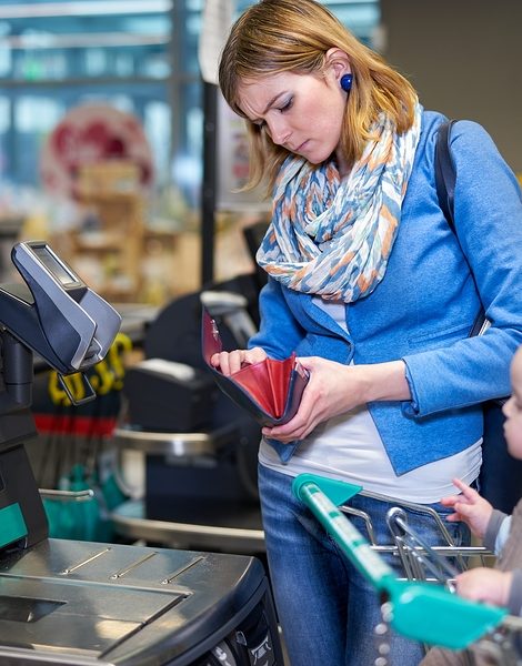 Young woman with toddler staying in front of self checkout machine and looking with serious face into her purse