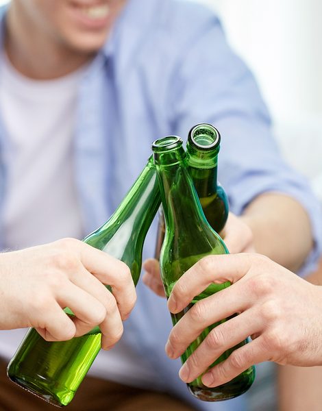 friendship, alcohol, people, celebration and holidays concept - close up of male friends drinking and clinking beer bottles at home