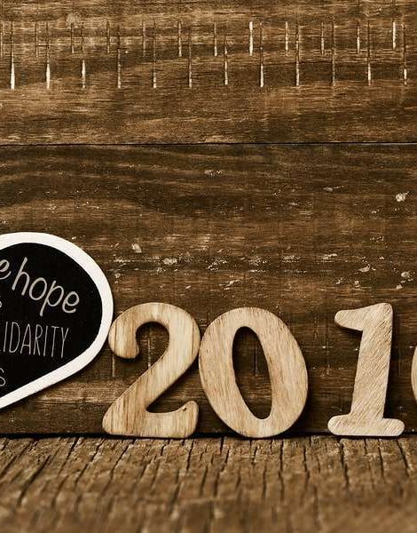 wooden numbers forming the number 2016 and a heart-shaped chalkboard with some wishes for the new year, such as peace, love and happiness, on a rustic wooden surface